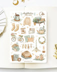 Premium Handmade Sticker Sheet
Aesthetic Cozy 105mm x 148mm - a sheet on the table with a white flower branch, an opened notebook
