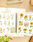 Premium Handmade Sticker Sheet Chamomile Sunflower 105mm x 148mm - 2 sheets on the table with a plant branch, an opened notebook