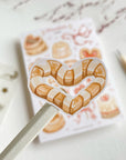 Premium Handmade Sticker Sheet
Chocolate Lover 105mm x 148mm - a piece and a sheet on the table with a dark maroon flower branch, a pencil in the background