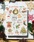 Premium Handmade Sticker Sheet Christmas 105mm x 148mm - a sheet on the table with a white flower branch, an opened notebook, 5 pinecones, 2 pine branches, 2 red berry branches, 5 stars