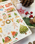 Premium Handmade Sticker Sheet Christmas 105mm x 148mm - a sheet on the table with an opened notebook, an acorn, a pinecone, 2 stars