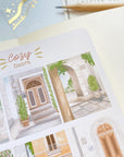 Premium Handmade Sticker Sheet Cozy Doors 105mm x 148mm - a sheet on the table with an opened notebook