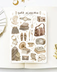 Premium Handmade Sticker Sheet Dark & Light Academia 105mm x 148mm - a sheet on the table with a white flower branch, an opened notebook