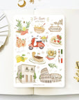 Premium Handmade Sticker Sheet In Love With Italy 105mm x 148mm - a sheet on the table with a white flower branch, an opened notebook