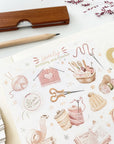 Premium Handmade Sticker Sheet Knitting Crochet 105mm x 148mm - a sheet on the table with a dark maroon flower branch, an opened notebook, a pencil, a ruler