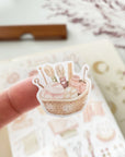 Premium Handmade Sticker Sheet Knitting Crochet 105mm x 148mm - a piece on the finger and a sheet on the table with a dark maroon flower branch, an opened notebook, a ruler