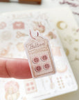 Premium Handmade Sticker Sheet Knitting Crochet 105mm x 148mm - a piece on the finger and a sheet on the table with a dark maroon flower branch, an opened notebook