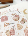 Premium Handmade Sticker Sheet Knitting Crochet 105mm x 148mm - a sheet on the table with a dark maroon flower branch, an opened notebook, a pencil, a ruler