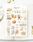 Premium Handmade Sticker Sheet Magical Cozy Fall 105mm x 148mm - a sheet on the table with a white flower branch, an opened notebook
