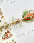 Premium Handmade Sticker Sheet Magical Cozy Winter 105mm x 148mm - 3 transparent pieces and a sheet on the table with an opened notebook