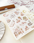 Premium Handmade Sticker Sheet Reading at Home 105mm x 148mm - a sheet on the table with a dark maroon flower branch, an opened notebook, a pencil, a ruler