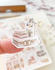 Premium Handmade Sticker Sheet Reading at Home 105mm x 148mm - a piece on the finger and a sheet on the table with a dark maroon flower branch, an opened notebook, a pencil, a ruler