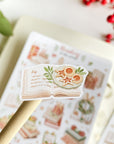 Premium Handmade Sticker Sheet
Reading in the Winter 105mm x 148mm - a piece and a sheet on the table with a branch, a red berry branch