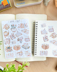 Premium Handmade Sticker Sheet Reading Time 105mm x 148mm - 9 pieces and a sheet on the table with a plant pot, an opened notebook