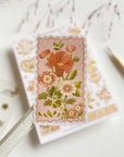 Premium Handmade Sticker Sheet Romantic Flower 105mm x 148mm - a piece and a sheet on the table with a pink flower branch in the background