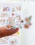 Premium Handmade Sticker Sheet Summer Breeze 105mm x 148mm - a piece on finger and a sheet on the table with an opened notebook