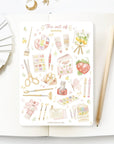 Premium Handmade Sticker Sheet The Art of Summer 105mm x 148mm - a sheet on the table with a pencil, an opened notebook