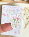 Premium Handmade Sticker Sheet Wild Flower 105mm x 148mm - a piece on the finger and a sheet on the table with a white flower branch, an opened notebook