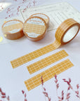 Premium Handmade Washi Tape Butterscotch Grid 15mm x 10m - 3 pieces and 4 washi tapes on the table with 2 dark maroon flower branches, a sticker sheet, a chapter heading