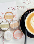 Premium Handmade Washi Tape Butterscotch Grid 15mm x 10m - 5 washi tapes on the table with 2 dark maroon flower branches, a sticker sheet, a chapter heading, a cup of latte with spoon