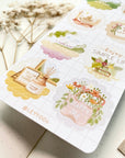 Premium Handmade Sticker Sheet A Day At Home 105mm x 148mm - a sheet on the table with a white flower branch, an opened notebook