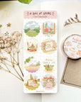 Premium Handmade Sticker Sheet A Day At Home 105mm x 148mm - a sheet on the table with a white flower branch, a purple flower branch, a washi tape, an opened notebook