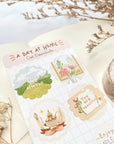 Premium Handmade Sticker Sheet A Day At Home 105mm x 148mm - a sheet on the table with a white flower branch, a purple flower branch, a washi tape, an opened notebook