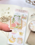 Premium Handmade Sticker Sheet A Day At Home 105mm x 148mm - a piece on the finger and a sheet on the table with a white flower branch, a purple flower branch, a washi tape, an opened notebook