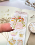Premium Handmade Sticker Sheet A Day At Home 105mm x 148mm - a piece on the finger and a sheet on the table with a white flower branch, a purple flower branch, a washi tape, an opened notebook