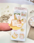 Premium Handmade Sticker Sheet A Day At Home 105mm x 148mm - a piece on the finger and a sheet on the table with a white flower branch, a purple flower branch, a washi tape, an opened notebook