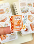 Premium Handmade Sticker Sheet Aesthetic Book 105mm x 148mm - a piece on the finger and 2 sheets on the table with an opened notebook