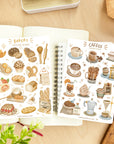 Premium Handmade Sticker Sheet Coffee 105mm x 148mm - 2 sheets on the table with a plant branch, an opened notebook