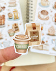 Premium Handmade Sticker Sheet Coffee 105mm x 148mm - a piece on the finger and 2 sheets on the table with an opened notebook