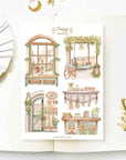 Premium Handmade Sticker Sheet Cozy Scenery 105mm x 148mm - 4 pieces on the table with a white flower branch, a opened notebook