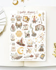Premium Handmade Sticker Sheet Dark Magic 105mm x 148mm - a sheet on the table with a white flower branch, an opened notebook