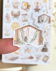 Premium Handmade Sticker Sheet Dark Magic 105mm x 148mm - a piece on the finger and a sheet on the table with a white flower branch, an opened notebook