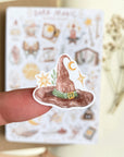 Premium Handmade Sticker Sheet Dark Magic 105mm x 148mm - a piece on the finger and a sheet on the table with a white flower branch, an opened notebook