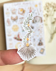 Premium Handmade Sticker Sheet Dark Magic 105mm x 148mm - a piece on the finger and a sheet on the table with a white flower branch, an opened notebook