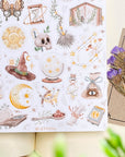 Premium Handmade Sticker Sheet Dark Magic 105mm x 148mm - a sheet on the table with a purple flower branch, an opened notebook