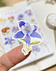 Premium Handmade Sticker Sheet Floral Desire 105mm x 148mm - a piece on the finger and a sheet on the table with a white flower branch, an opened notebook, a washi tape