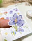 Premium Handmade Sticker Sheet Floral Desire 105mm x 148mm - a piece on the finger and a sheet on the table with a white flower branch, an opened notebook, a washi tape