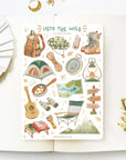 Premium Handmade Sticker Sheet Into The Wild 105mm x 148mm - a sheet on the table with a white flower branch, an opened notebook
