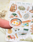 Premium Handmade Sticker Sheet Into The Wild 105mm x 148mm - a piece on the finger and a sheet on the table with a white flower branch, an opened notebook