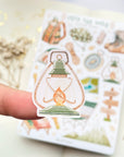 Premium Handmade Sticker Sheet Into The Wild 105mm x 148mm - a piece on the finger and a sheet on the table with a white flower branch, an opened notebook