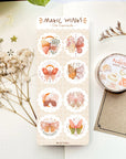 Premium Handmade Sticker Sheet Magic Wings 105mm x 148mm - a sheet on the table with a white flower branch, a purple flower brand, an opened notebook, a golden sticker sheet, a washi tape