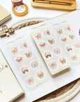 Premium Handmade Sticker Sheet Magic Wings 105mm x 148mm - 3 sheets on the table with a white branch, an opened notebook, a purple flower branch, a washi tape, a tape, a pen with box