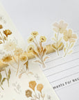 Premium Handmade Sticker Sheet Mellow Flower 105mm x 148mm - 3 pieces on the stick and a piece on the finger and a sheet on the table with an opened notebook