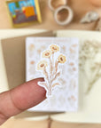 Premium Handmade Sticker Sheet Mellow Flower 105mm x 148mm - a piece on the finger and a sheet on the table with a white flower branch, an opened notebook