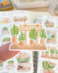 Premium Handmade Sticker Sheet Spring Garden 105mm x 148mm - a piece on the finger and 2 sheets on the table with a rabbit statue, an opened notebook