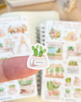 Premium Handmade Sticker Sheet Spring Garden 105mm x 148mm - a piece on the finger and 2 sheets on the table with a rabbit statue, an opened notebook